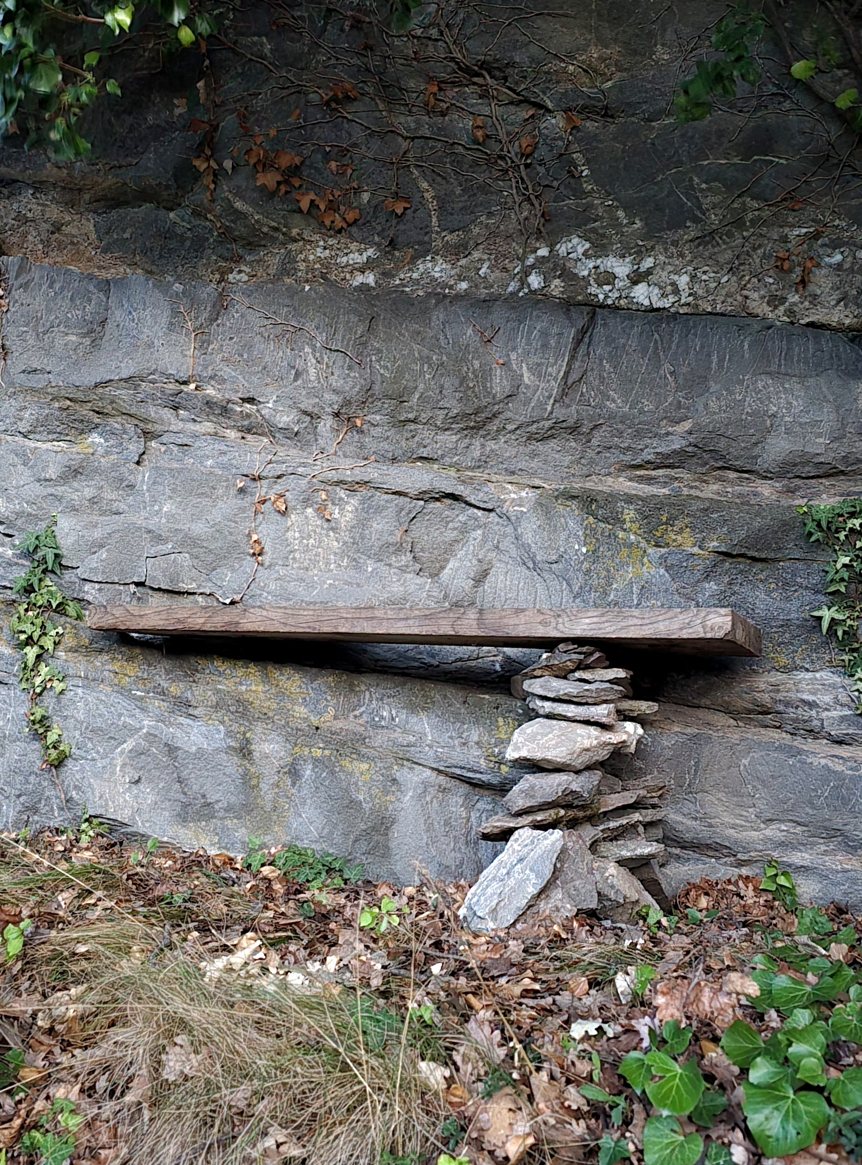 Banc en bois posé sur des pierres sèches contre une paroi rocheuse à Champlan en automne.